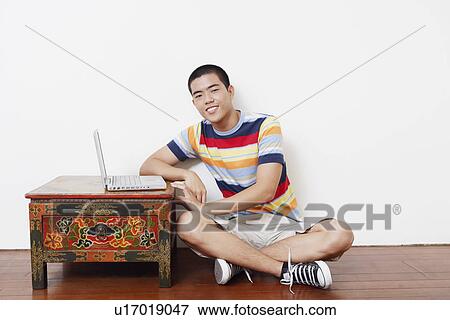 Portrait of a young man sitting on the floor with a laptop on the table View Large Photo Image Stock Photo - Portrait of a young man sitting on the floor with a laptop on the table. Fotosearch