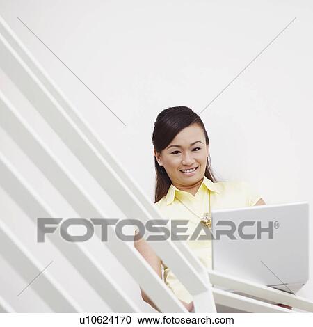 Stock Image - Portrait of a young woman using a laptop and smiling. Fotosearch