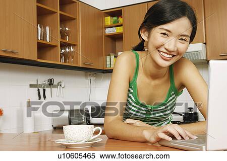 Portrait of a young woman using a laptop at a kitchen counter View Large Photo Image Stock Photography - Portrait of a young woman using a laptop at a kitchen counter. Fotosearch