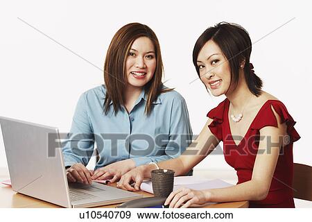 Stock Photo - Portrait of two businesswomen sitting in front of a laptop. Fotosearch