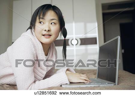 Stock Image - Side profile of a young woman using a laptop. Fotosearch