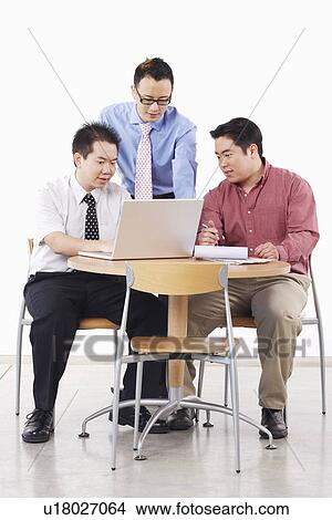 Picture - Three businessmen discussing in front of a laptop. Fotosearch