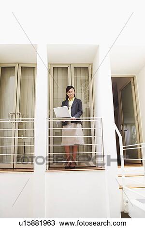 Young woman standing at a doorway of an office and using a laptop View Large Photo Image Stock Image - Young woman standing at a doorway of an office and using a laptop. Fotosearch