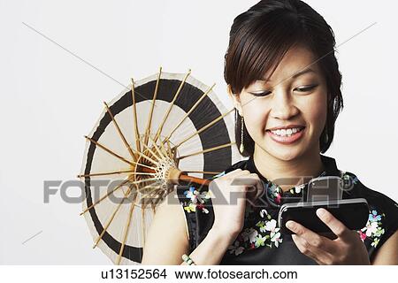 Close-up of a young woman holding a parasol looking at a mobile phone View Large Photo Image Picture - Close-up of a young woman holding a parasol looking at a mobile phone. Fotosearch