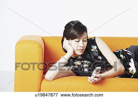 Stock Photo - Close-up of a young woman lying on a couch looking at a mobile phone. Fotosearch
