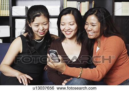 Stock Photograph - Close-up of three friends looking at a mobile phone smiling. Fotosearch