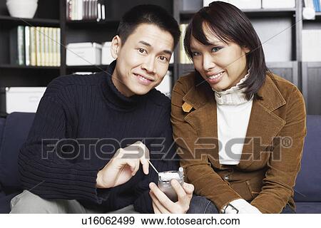 Portrait of a young man sitting with a young woman on a couch holding a mobile phone View Large Photo Image Stock Photo - Portrait of a young man sitting with a young woman on a couch holding a mobile phone. Fotosearch