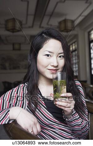 Stock Image - Portrait of a young woman holding a glass of herbal drink. Fotosearch
