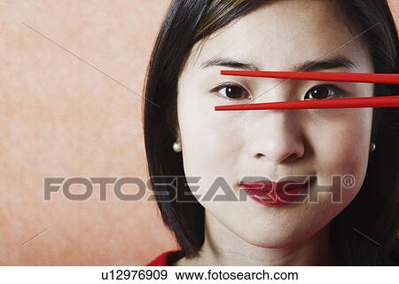 Stock Photo - Portrait of a young woman looking through chopsticks. Fotosearch