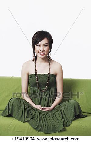Picture - Portrait of a young woman sitting cross-legged on a couch. Fotosearch