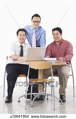 Portrait of three businessmen smiling in front of a laptop View Large Photo Image Picture - Portrait of three businessmen smiling in front of a laptop. Fotosearch
