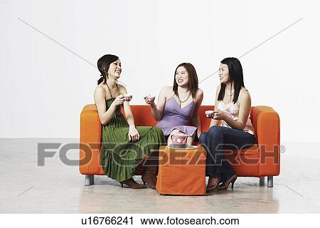 Stock Image - Three young women sitting on a couch with tea cups. Fotosearch