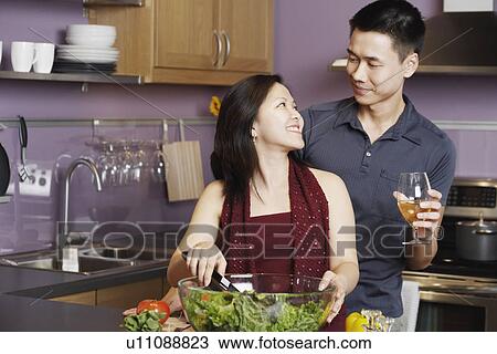 Young man standing holding a wineglass with a young woman preparing food View Large Photo Image Stock Image - Young man standing holding a wineglass with a young woman preparing food. Fotosearch