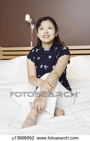 Stock Image - Young woman sitting on the bed thinking. Fotosearch