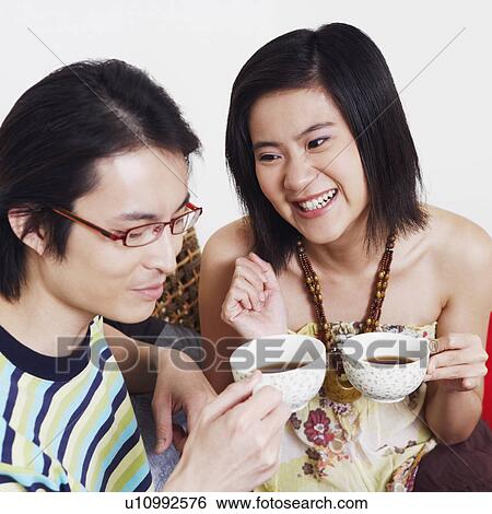 Stock Photograph - Close-up of a mid adult man and a young woman holding cups of tea and smiling. Fotosearch