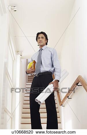 Low angle view of a male architect holding rolled up blueprints and a hardhat View Large Photo Image Stock Image - Low angle view of a male architect holding rolled up blueprints and a hardhat. Fotosearch