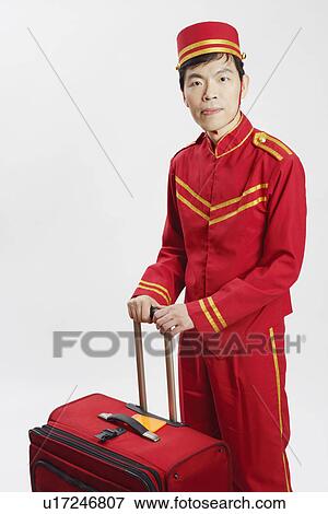 Stock Photo - Portrait of a bellhop standing with a suitcase. Fotosearch