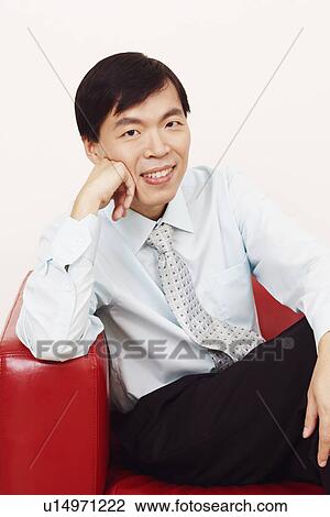 Stock Image - Portrait of a businessman sitting on a couch and smiling. Fotosearch