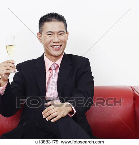 Portrait of a businessman sitting on a couch and holding a champagne flute View Large Photo Image Stock Photo - Portrait of a businessman sitting on a couch and holding a champagne flute. Fotosearch