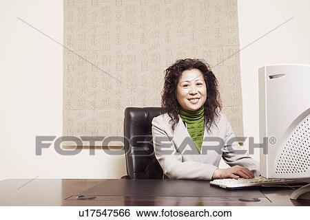 Stock Photograph - Portrait of a businesswoman sitting in front of a computer smiling. Fotosearch