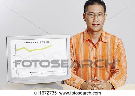 Portrait of a mid adult man sitting at a desk with a computer monitor showing financial status of a company View Large Photo Image Stock Photography - Portrait of a mid adult man sitting at a desk with a computer monitor showing financial status of a company. Fotosearch