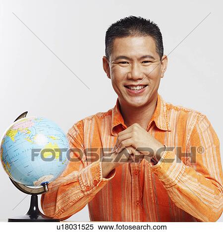 Stock Photography - Portrait of a mid adult man smiling and sitting besides a desktop globe. Fotosearch