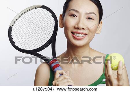 Stock Photo - Portrait of a mid adult woman holding a tennis ball and a tennis racket. Fotosearch