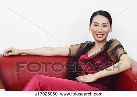 Portrait of a mid adult woman sitting on a couch and smiling View Large Photo Image Stock Image - Portrait of a mid adult woman sitting on a couch and smiling. Fotosearch