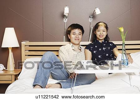 Stock Image - Portrait of a young man and a mid adult woman on the bed. Fotosearch