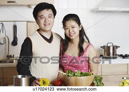 Stock Image - Portrait of a young man standing with a mid adult woman in the kitchen. Fotosearch