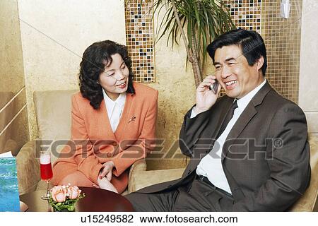 Stock Image - Businessman sitting with a businesswoman in a restaurant talking on a mobile phone. Fotosearch