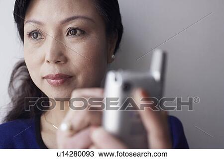 Stock Image - Close-up of a mature woman holding a mobile phone thinking. Fotosearch