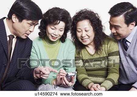 Close-up of two mature couples sitting together looking at a mobile phone View Large Photo Image Picture - Close-up of two mature couples sitting together looking at a mobile phone. Fotosearch