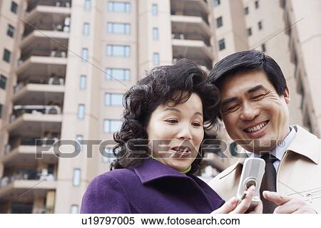 Low angle view of a mature couple looking at a mobile phone smiling View Large Photo Image Stock Photography - Low angle view of a mature couple looking at a mobile phone smiling. Fotosearch
