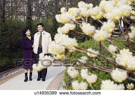 Stock Photo - Mature couple walking together in a garden smiling. Fotosearch