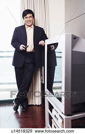 Stock Photo - Portrait of a businessman holding a remote control smiling. Fotosearch