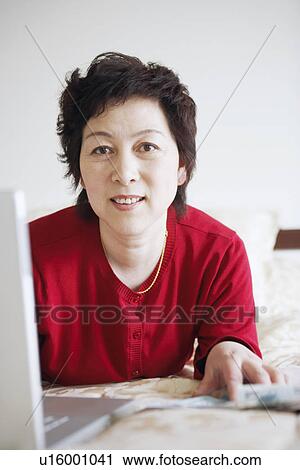 Stock Image - Portrait of a mature woman lying in front of a laptop. Fotosearch