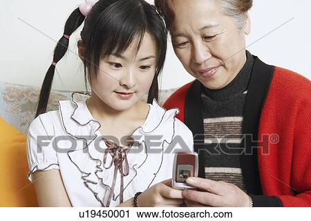 Close-up of a young woman sitting together with her grandmother holding a mobile phone View Large Photo Image Stock Image - Close-up of a young woman sitting together with her grandmother holding a mobile phone. Fotosearch