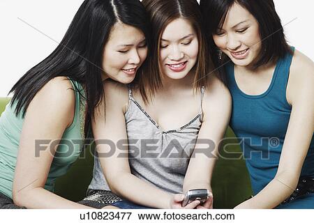 Stock Photo - Close-up of three young women holding a mobile phone. Fotosearch