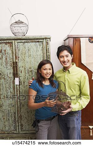 Stock Photography - Portrait of a young couple holding a cage and smiling. Fotosearch