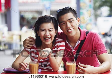 Stock Photograph - Portrait of a young couple sitting at a sidewalk cafe and smiling. Fotosearch