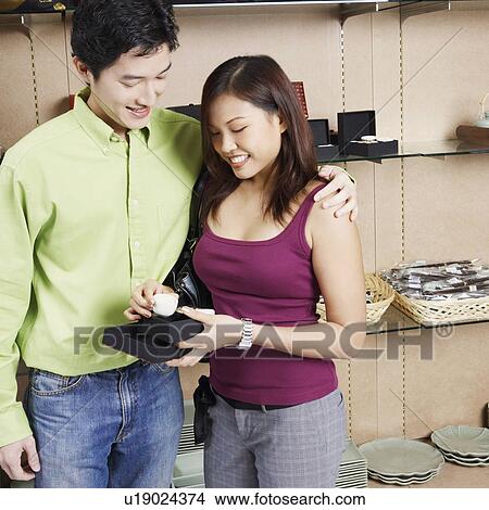 Picture - Young couple looking at a cup in a store and smiling. Fotosearch