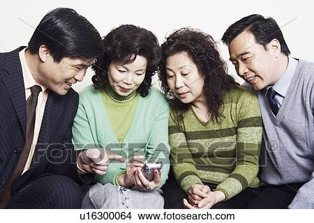 Picture - Close-up of two mature couples sitting together looking at a mobile phone. Fotosearch