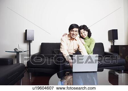 Stock Photo - Portrait of a mature man sitting on a couch with a mature woman using a laptop. Fotosearch