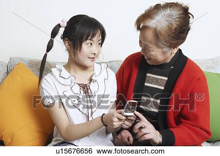 Stock Photograph - Young woman facing her grandmother holding a mobile phone. Fotosearch