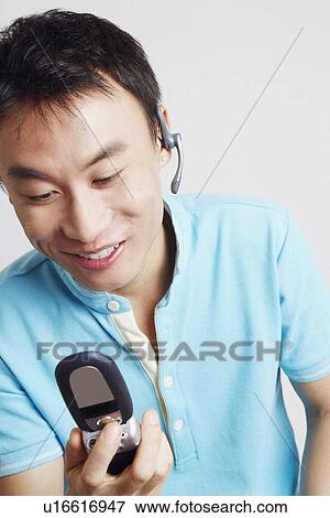 Close-up of a young man holding a mobile phone and smiling View Large Photo Image Stock Photo - Close-up of a young man holding a mobile phone and smiling. Fotosearch