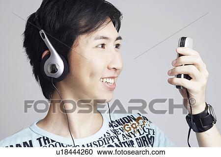 Close-up of a young man wearing headphones and holding a mobile phone View Large Photo Image Stock Image - Close-up of a young man wearing headphones and holding a mobile phone. Fotosearch