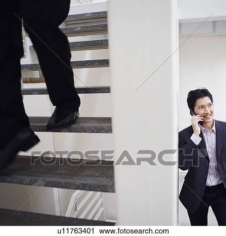Stock Image - Low section view of a man walking down stairs with another businessman talking on a mobile phone. Fotosearch
