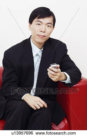 Stock Photograph - Portrait of a businessman sitting on a couch and holding a mobile phone. Fotosearch