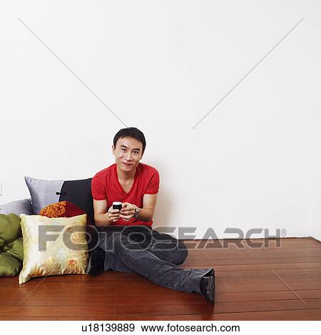 Portrait of a mid adult man sitting on the floor and holding a mobile phone View Large Photo Image Stock Photo - Portrait of a mid adult man sitting on the floor and holding a mobile phone. Fotosearch